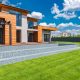 Exterior of contemporary residential house with panoramic windows glass doors and green lawn in yard on sunny day against blue sky with white clouds